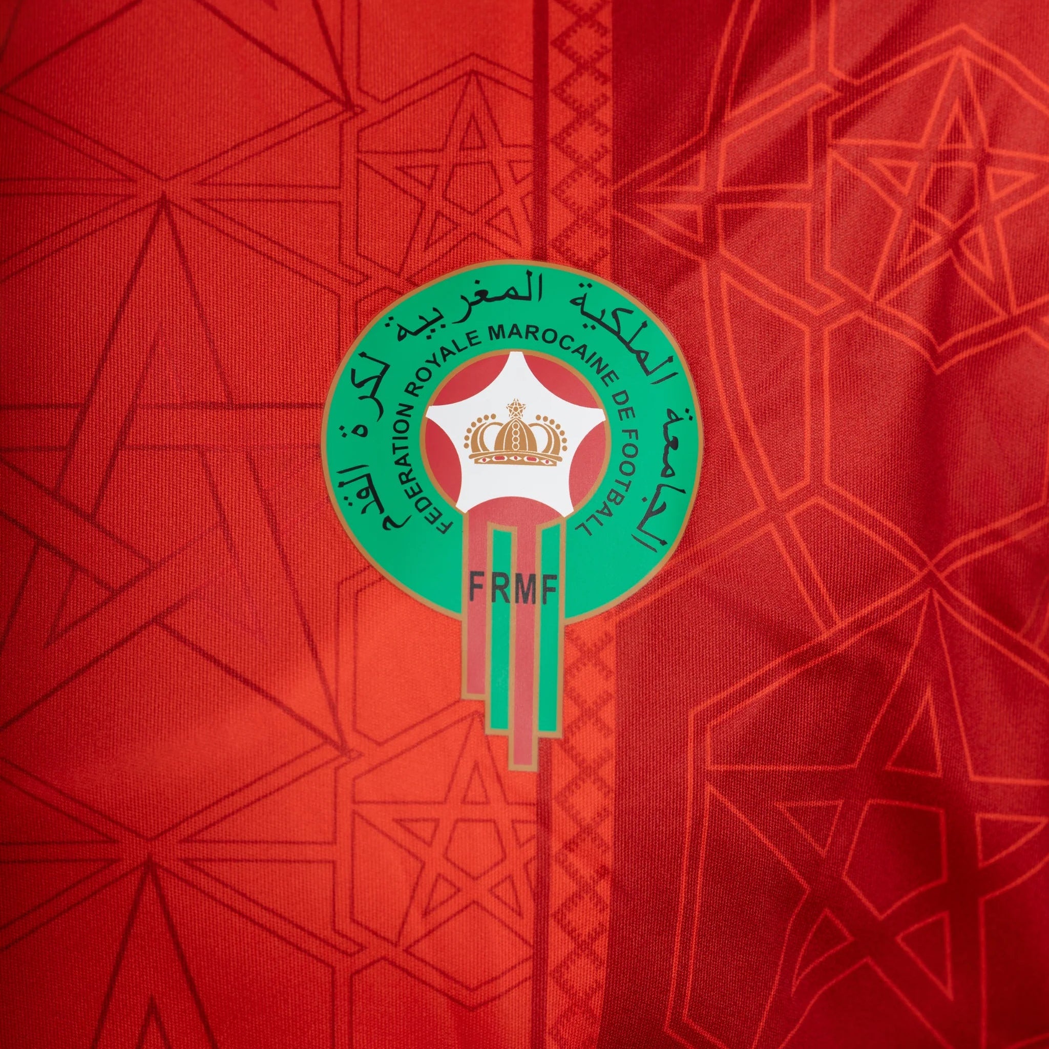 Red sports jersey with a green and white emblem featuring Arabic text and a star design.