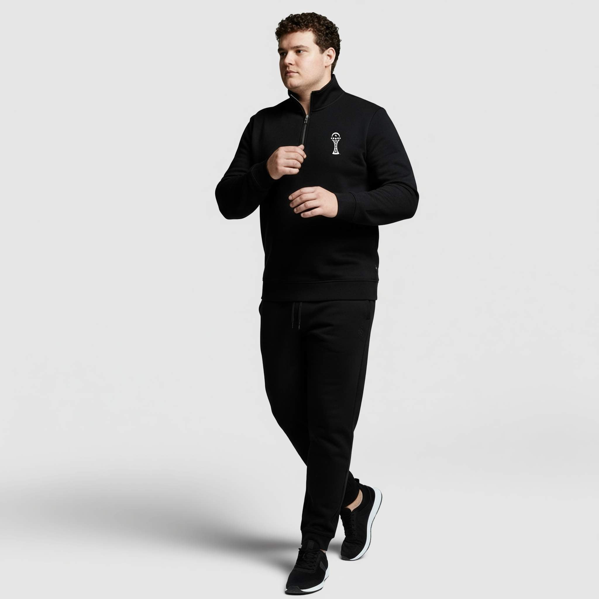 Man wearing a black tracksuit with a logo on a light gray background